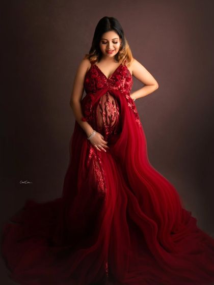 This full-length portrait showcases a gorgeous mom-to-be in a detailed red gown with a sheer, embroidered mid-section that beautifully displays her bump.