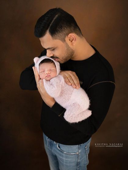A father's gentle kiss for his newborn daughter. This tender moment, with the baby dressed in a pink bear outfit, is incredibly sweet and heartwarming.