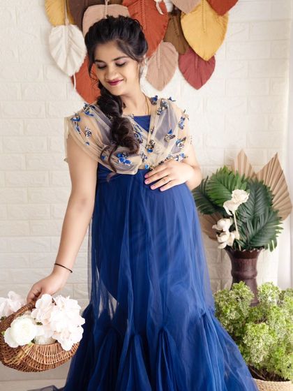 A sweet and gentle portrait of a mom-to-be in a blue gown, holding a basket of white flowers in a bright studio setting.