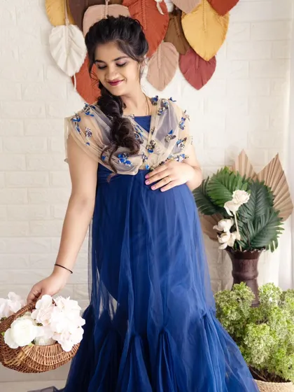 A sweet and gentle portrait of a mom-to-be in a blue gown, holding a basket of white flowers in a bright studio setting.
