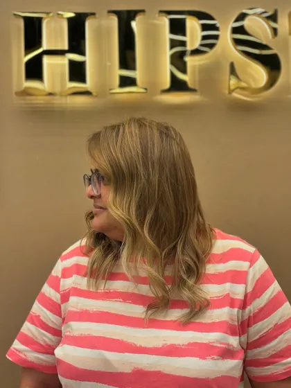 A side view of a client's fresh blonde hair color, styled with soft waves to showcase the new look.