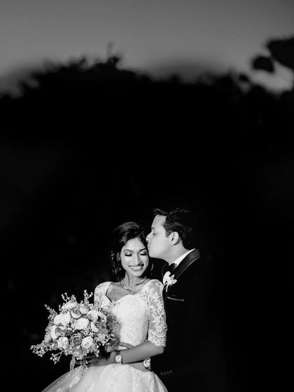 A beautiful black and white portrait against a dark background. The groom's kiss and the bride's smile are the focal points of this intimate shot.