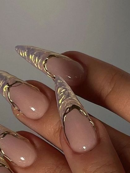 A close-up of extremely long, clear stiletto extensions. The tips are adorned with a 3D gold textured design, creating a look that is both delicate and fierce.