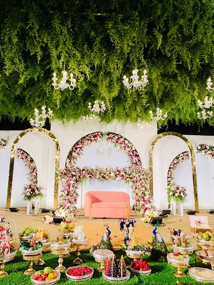 We designed this reception stage to feel like an enchanted garden. A lush ceiling of suspended greenery and dozens of crystal chandeliers creates a luxurious canopy over a stage adorned with floral arches and elegant seating, showcasing how we transform large spaces into intimate wonderlands.