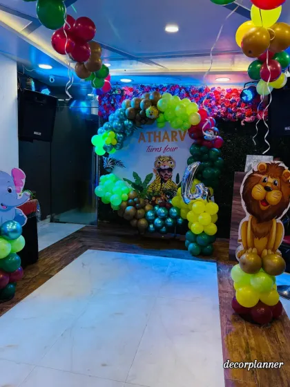 Another view of the jungle party setup, showing the main backdrop and character standees. The lighting in the venue enhances the colors of the balloons, creating a vibrant and exciting atmosphere.