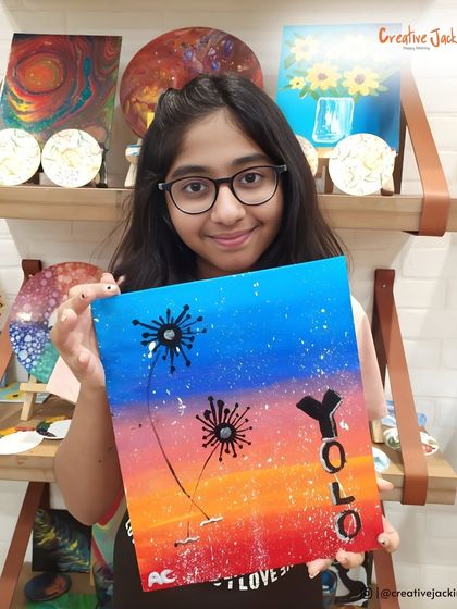 A young artist displays her colorful dandelion painting with the word "YOLO," showing her unique personality and creativity.