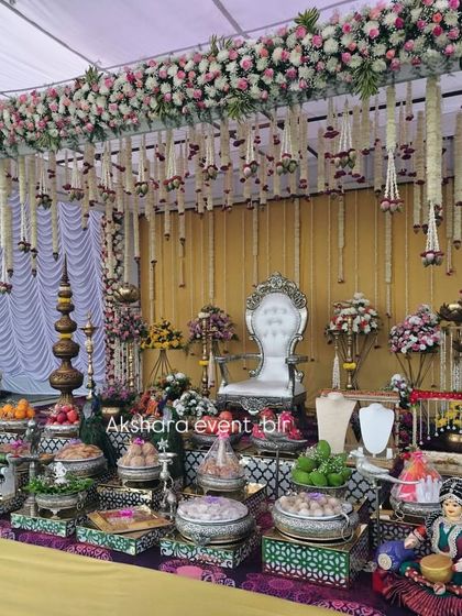 An elegant outdoor Seemantham setup with a canopy of flowers. The stage is filled with an elaborate display of offerings, traditional dolls, and a silver throne for the mother-to-be.