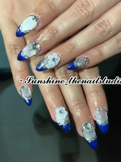 A detailed set with blue French tips, 3D flowers, and rhinestones.