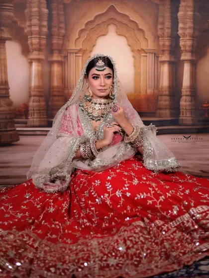 A full-length seated portrait, showing the beautiful spread of the embroidered red lehenga.
