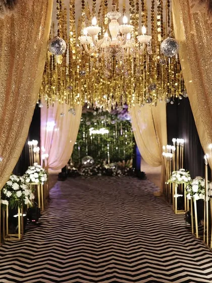 A glamorous entrance tunnel with gold sequin drapes, chandeliers, and a modern black and white carpet.