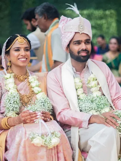 A happy portrait of the couple during their wedding ceremony. The soft pastel outfits and delicate floral garlands complement the elegant and serene decor.