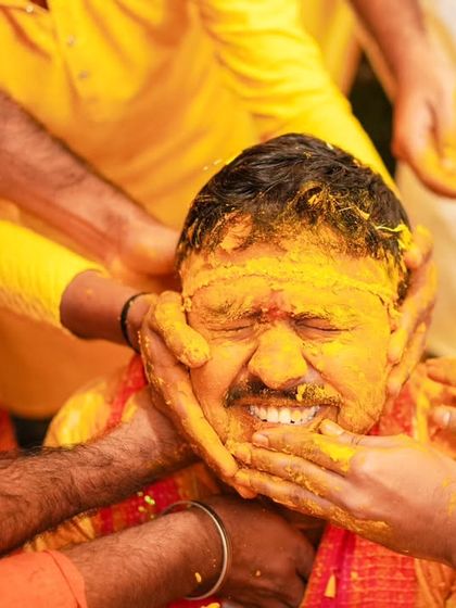 All hands in! A classic Haldi moment, showing the groom being lovingly covered in turmeric by his friends and family.