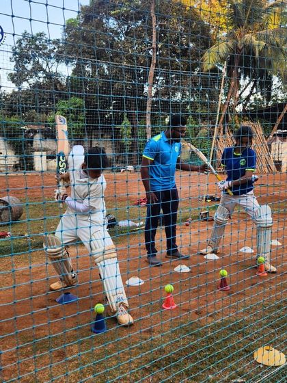 A young cricketer practices his batting form in the nets under the guidance of a coach. We use cones and markers to ensure precise technique development during our skill-focused sessions.
