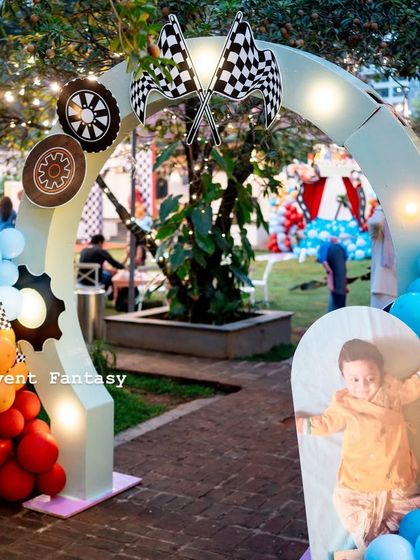 A welcoming arch for Lakhit's racing party, decorated with gears, checkered flags, and colorful balloons. A framed photo of the birthday boy adds a personal touch.