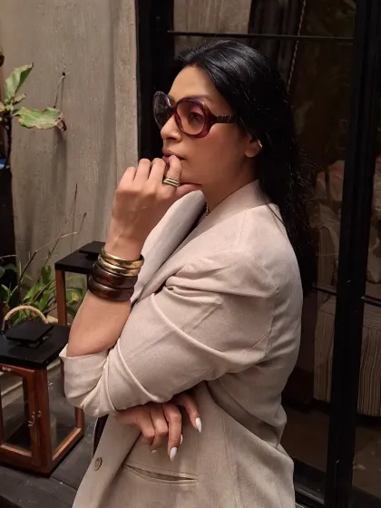 The side profile shows the texture of the linen blazer and the bold shape of the sunglasses.