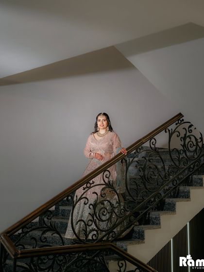 A striking portrait of the bride standing on a staircase with an ornate railing, creating a dramatic and elegant composition.