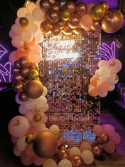 A close-up of the rose gold and pink balloon arch against the shimmering sequin backdrop. The addition of small butterfly decals adds a whimsical and delicate touch to the overall design.