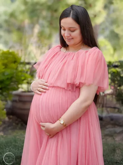 A gentle and serene outdoor portrait. The mother-to-be looks down at her bump with a soft smile, surrounded by the beauty of nature.