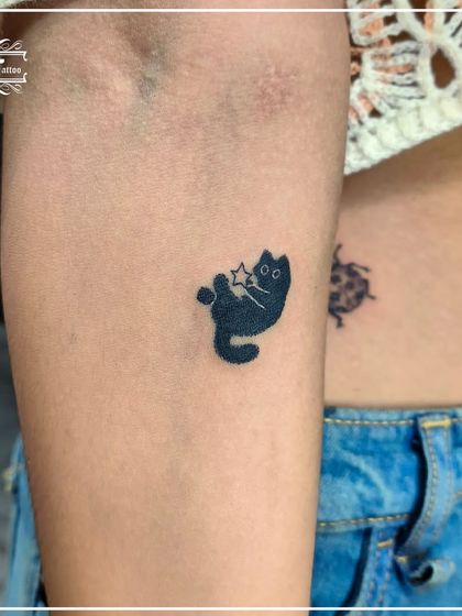 A playful and cute black cat tattoo holding a star. This solid black design shows that minimalist tattoos can also be bold and full of character.