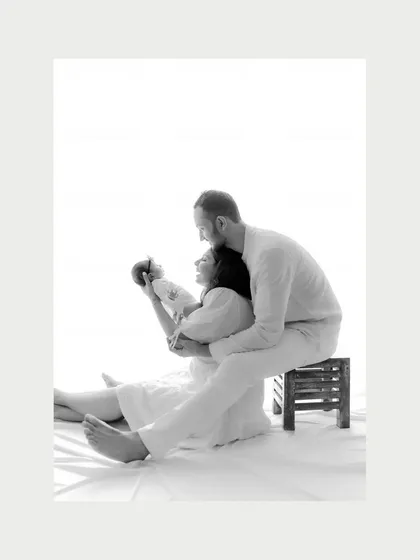 A beautifully composed black and white portrait of new parents with their baby. The mother holds the newborn while seated, supported by the father, creating a strong and loving family unit. The image feels both artistic and deeply personal.