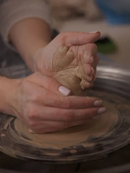 Hands pressing into a lump of clay on the wheel, the very first step of centering before pulling up the walls.