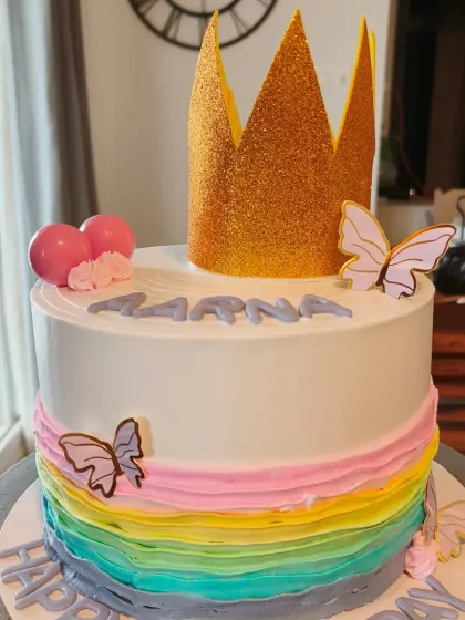 A beautiful rainbow layer cake topped with a glittering gold crown and butterflies.
