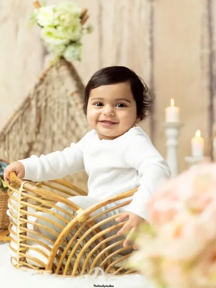 A sweet smile from the birthday boy, sitting in a wicker basket surrounded by soft lighting and props.