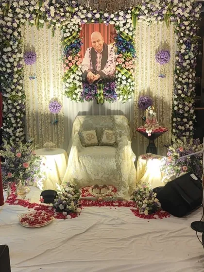 This is a close-up of a gaddi setup where the portrait of Guru Ji is framed by a rich arrangement of roses, carnations, and hydrangeas in shades of purple, blue, and white.