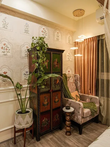 A cozy reading nook in a bedroom with a hand-painted cabinet and floral armchair, showcasing a blend of ethnic and classic styles.