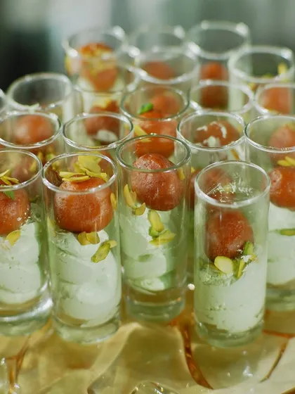 A modern fusion dessert: Gulab Jamun served in a shot glass with a light and airy pistachio cream. This combines a beloved traditional sweet with a contemporary presentation.