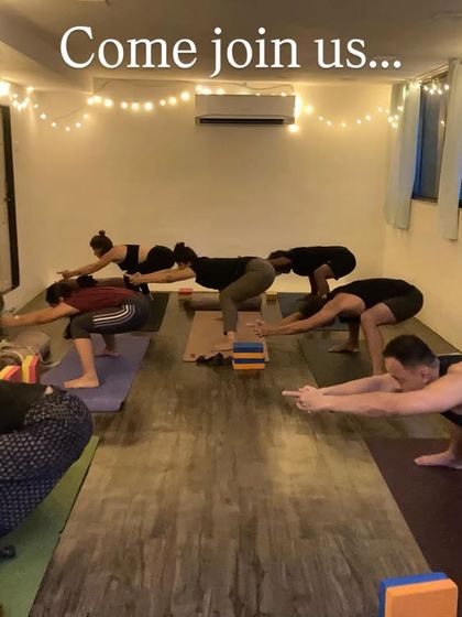 Come join us. A welcoming image of our group class in a chair pose variation, using the energy of the room to find strength and stability.