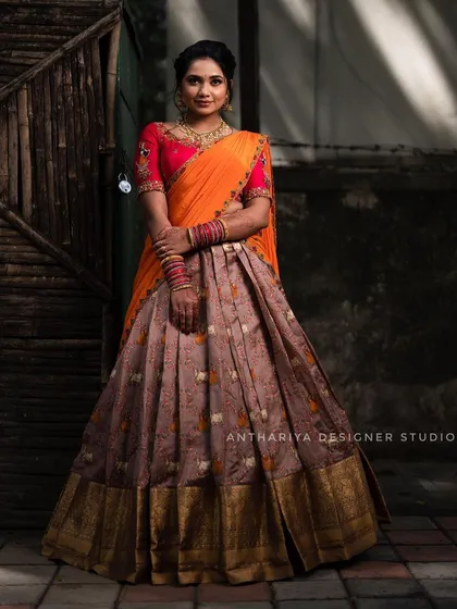 We offer traditional South Indian attire for rent, like this beautiful half saree. The outfit combines a mauve printed skirt with a rich gold border and a vibrant orange and pink embroidered blouse.