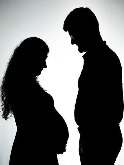 A beautiful silhouette of a couple looking down at the baby bump. It's a quiet, intimate moment frozen in time.