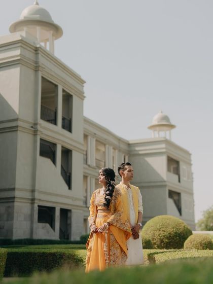 A stylish portrait of Mehul and Divya at their Haldi ceremony. Their coordinated yellow outfits and the grand architecture create a regal and fashionable look.