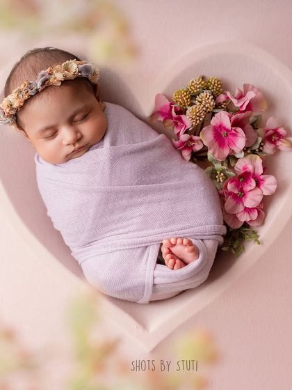 A newborn nestled in a heart-shaped bowl, surrounded by pink flowers. This is a popular and heartwarming setup that symbolizes all the love you have for your new baby.