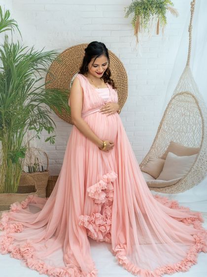 A full-length portrait of a mom-to-be in a pink ruffled gown, looking down at her bump in our beautiful boho studio.