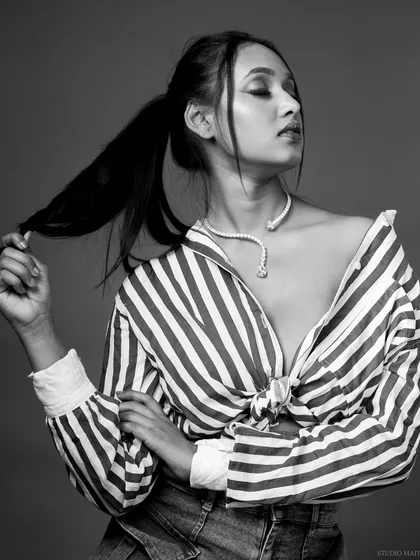 A moody black and white portrait. The off-the-shoulder striped shirt and pose create a relaxed yet stylish editorial look.