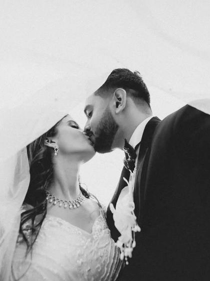 A classic and romantic black and white portrait, with the couple kissing under the bride's veil. The composition is intimate and timeless.