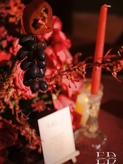 An artistic detail from the red-themed centerpiece, showing grapes and a sliced bell pepper hanging delicately amidst the floral arrangement.
