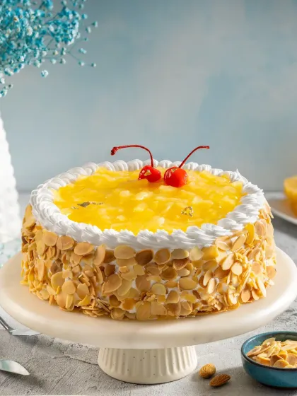 A classic pineapple pastry cake adorned with almond flakes and cherries, presented on a cake stand for a bright and inviting product shot.
