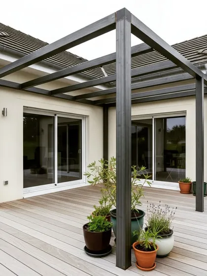 A minimalist black metal pergola installed on a light-colored wooden deck. The clean lines and open-frame design complement the modern architecture of the home.