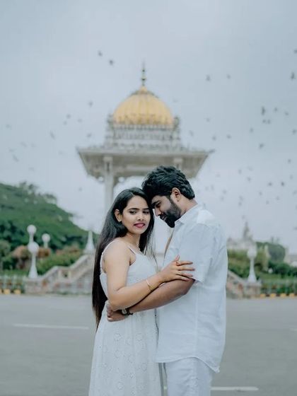 A romantic pre-wedding portrait in front of a Mysore landmark, with birds flying in the background, adding a magical, spontaneous element to the shot.