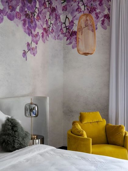 A luxurious bedroom in a Mysuru home, where a custom wallpaper of purple orchids and a vibrant yellow armchair create a bold and elegant statement.