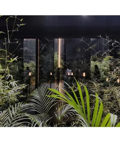 Looking out from the Black Pavilion into the garden it frames. The dark, porous mesh walls create a stark contrast with the vibrant green of the plants, heightening the sense of being in a sanctuary.