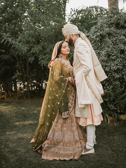 A full-length portrait of the couple in a lush garden setting. The groom’s gentle kiss on his bride's forehead creates a timeless and romantic image.