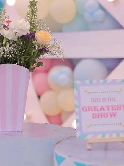 A simple yet beautiful floral centerpiece in a pink and white striped vase. The "This is the Greatest Show" sign on a mini easel reinforces the carnival theme in a subtle and elegant way.