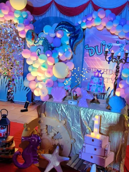 The mermaid theme under party lights, creating a magical underwater glow with iridescent balloons and a shimmer wall.