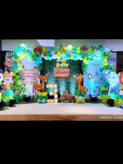 A detailed jungle theme stage for a 3rd birthday. This setup includes a green wall backdrop, 3D animal cutouts, and a light-up marquee number, creating a wild adventure.