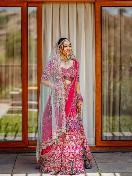 A vision in pink! This stunning full-length portrait showcases the intricate details of the bride's vibrant lehenga. Her happy and confident smile truly lights up the frame.