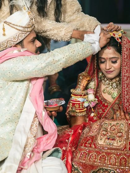 The groom applying sindoor to the bride's forehead, a significant ritual in a Hindu wedding. The focus is on the action and the couple's connection.
